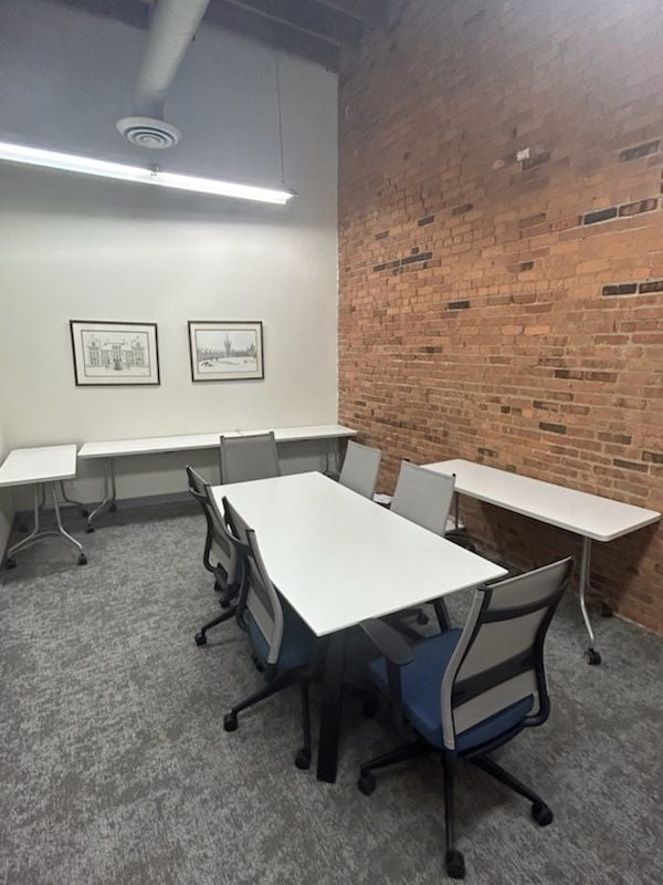 A conference room with exposed brick on one side, and several tables and chairs.